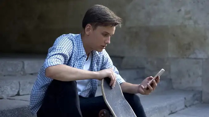 Dreng med skateboard kigger overrasket på sin mobil